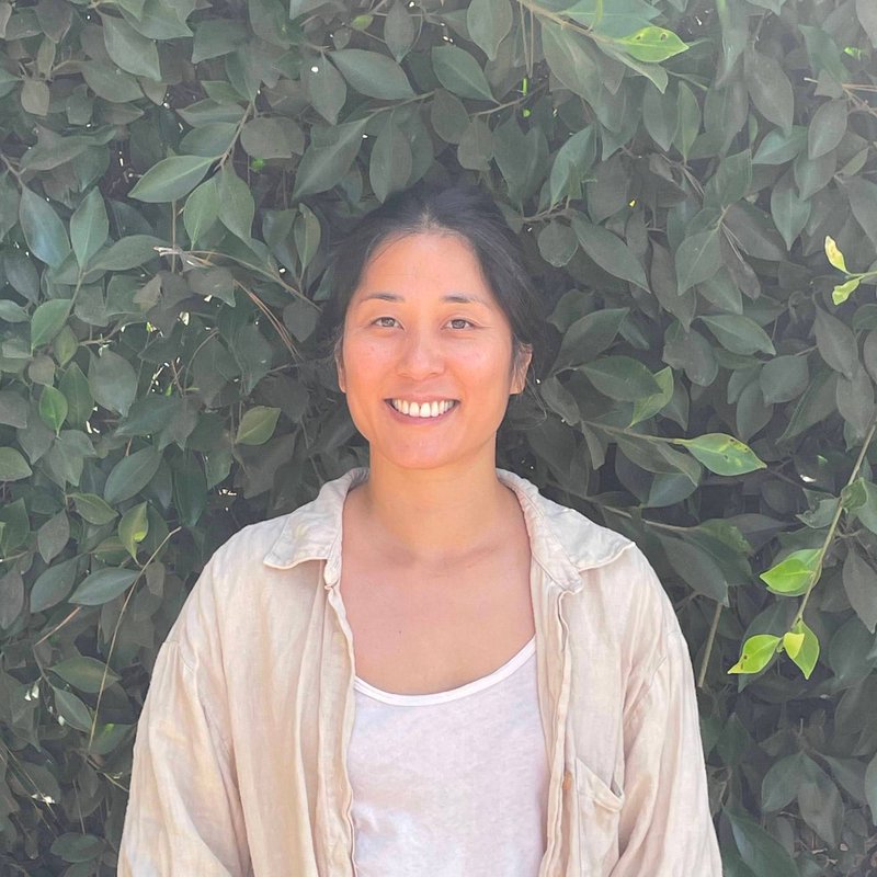 Tiffany Ho smiling in front of a leafy green hedge